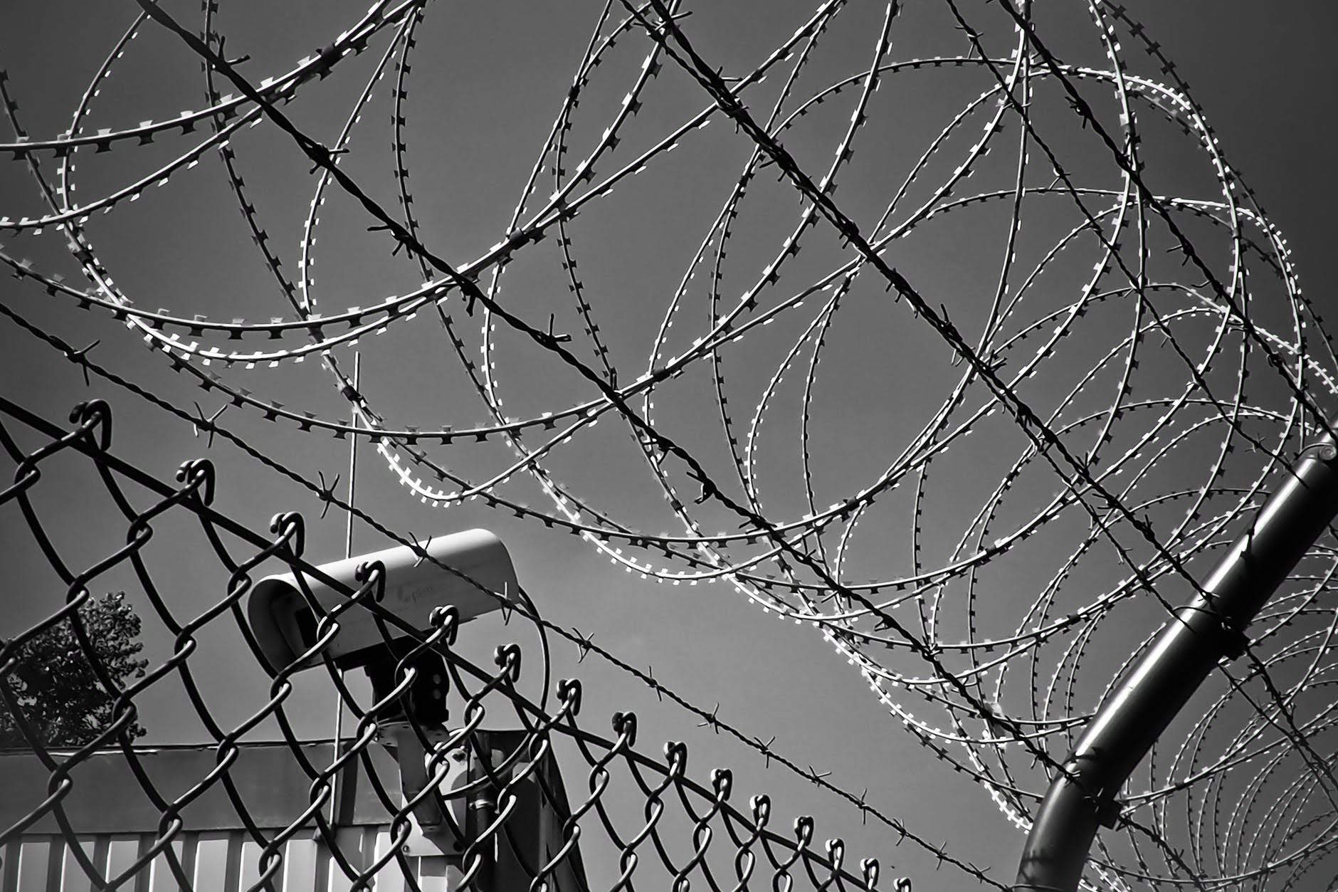 black and white image of barbed wire on fence and security camera