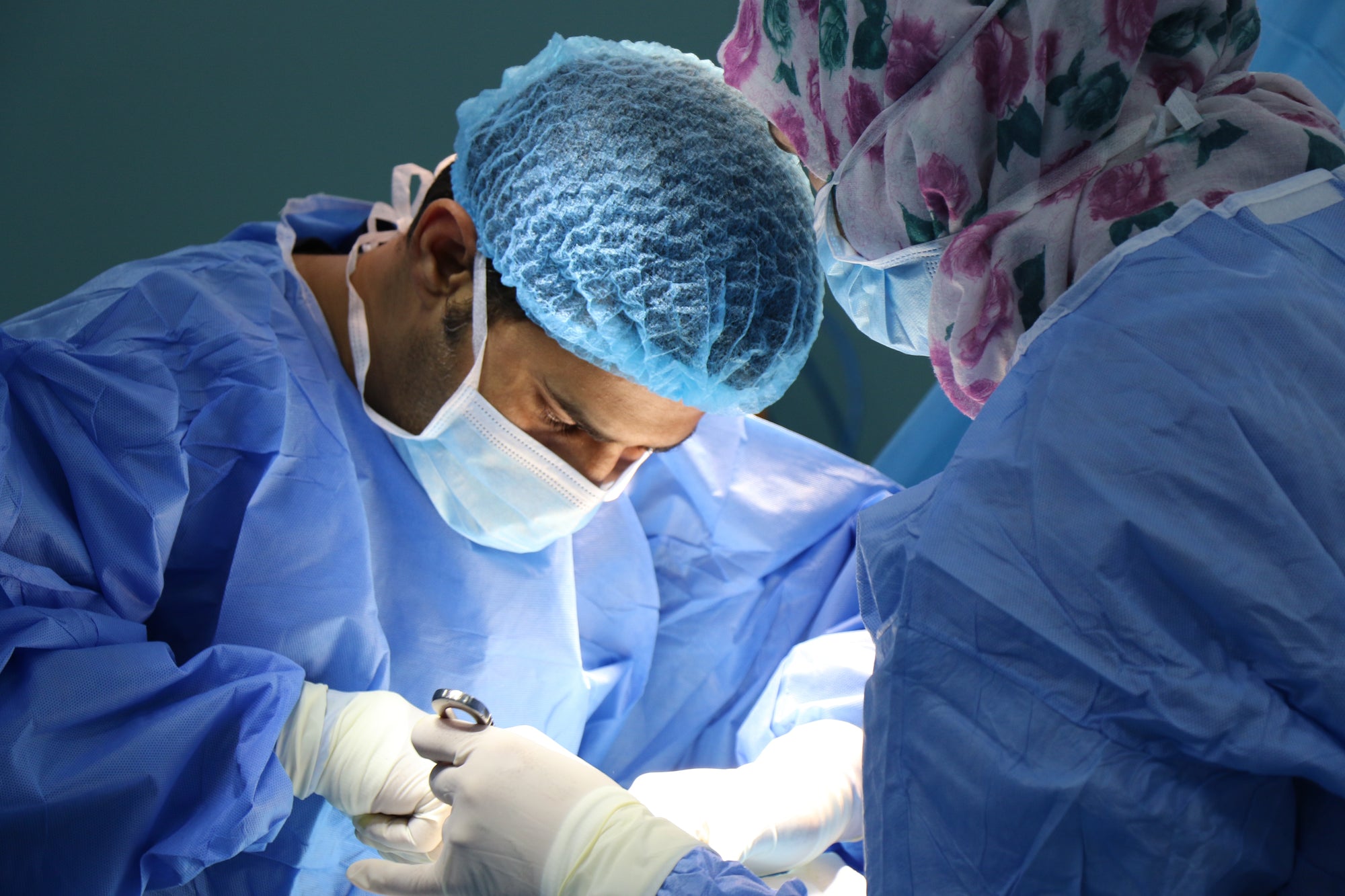 A doctor performing surgery in a mask and hair cap