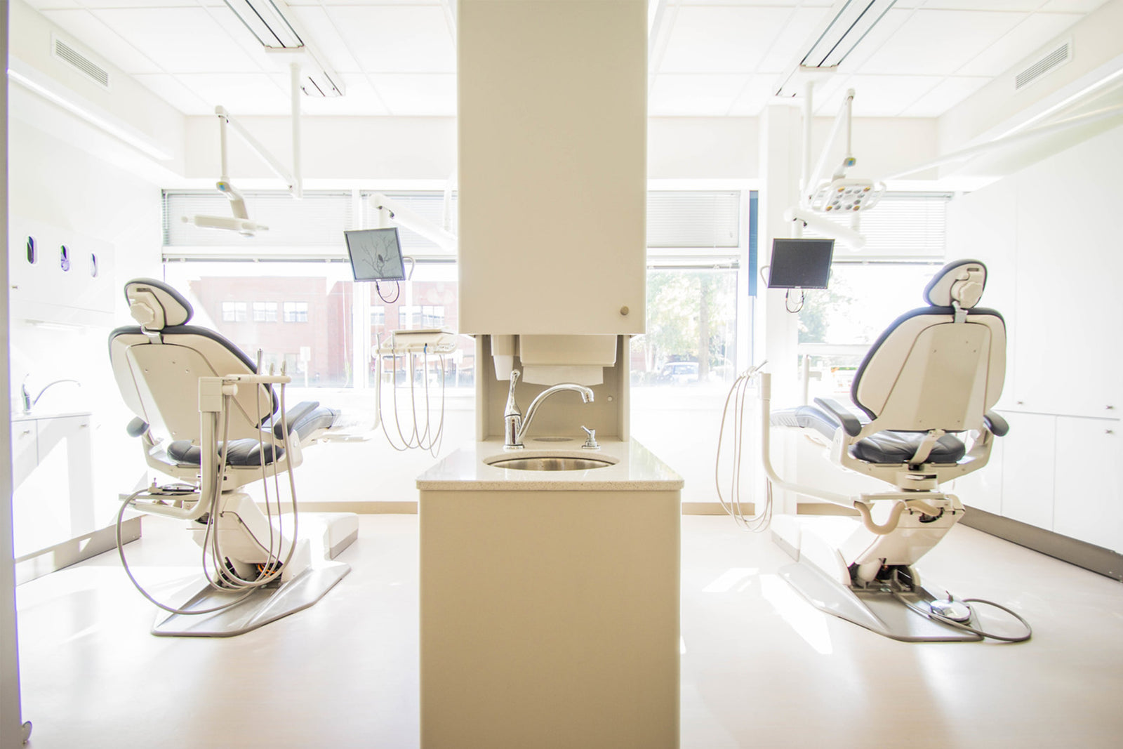 A white room with two dental chairs and a sink in between