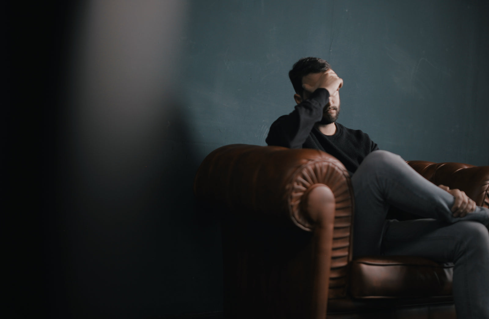 Distressed man sits on a brown sofa