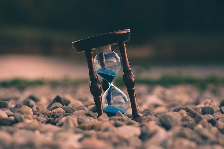 hourglass with blue sand falling through it sitting on a bed of rocks