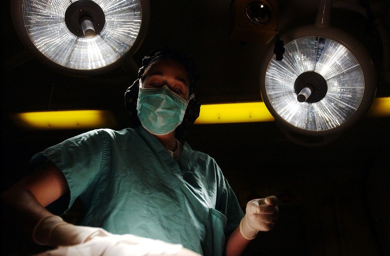 a doctor in scrubs and a mask holding a scalpel, as seen from what would be the patient's perspective during surgery